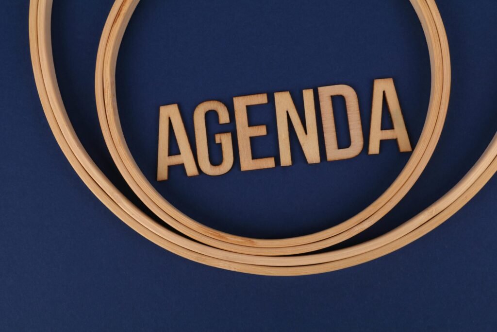 Wooden letters form the word 'AGENDA' encircled by hoops on a blue surface, suggesting planning and strategy.