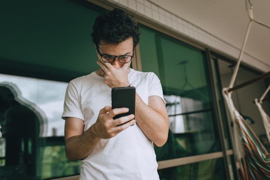 Man with eyeglasses focused on smartphone indoors, captured in a contemplative moment. golpe