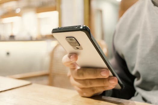 A person using a smartphone in a modern indoor setting, emphasizing technology. melhores ias