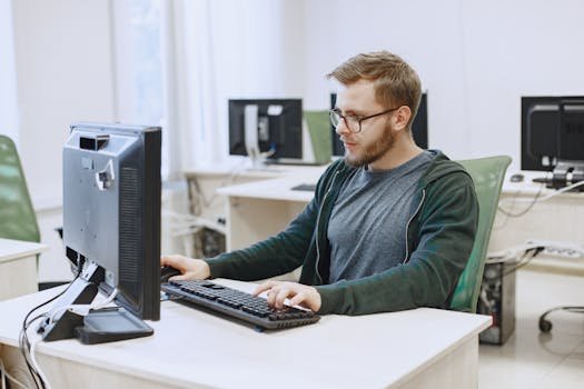 Young man with eyeglasses working on a desktop computer in a modern office environment. profissões