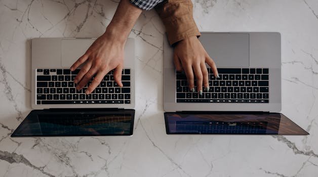 Two individuals typing on laptops from a top view angle, showcasing collaborative work. claude