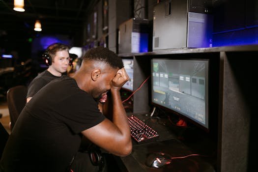 Two adult men experiencing disappointment while playing PC games in a modern indoor gaming arcade setting. antivírus
