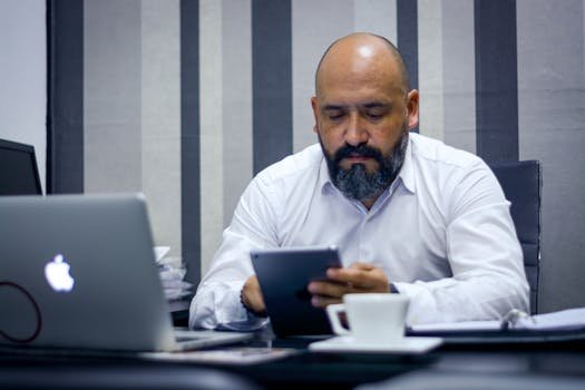 Bearded man using a tablet in a modern office environment, focusing on technology and productivity. portfólio