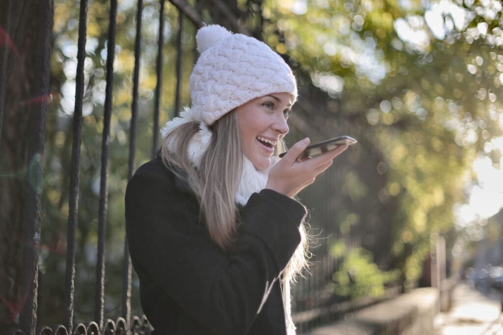 Smiling young woman using smartphone outdoors in winter attire.