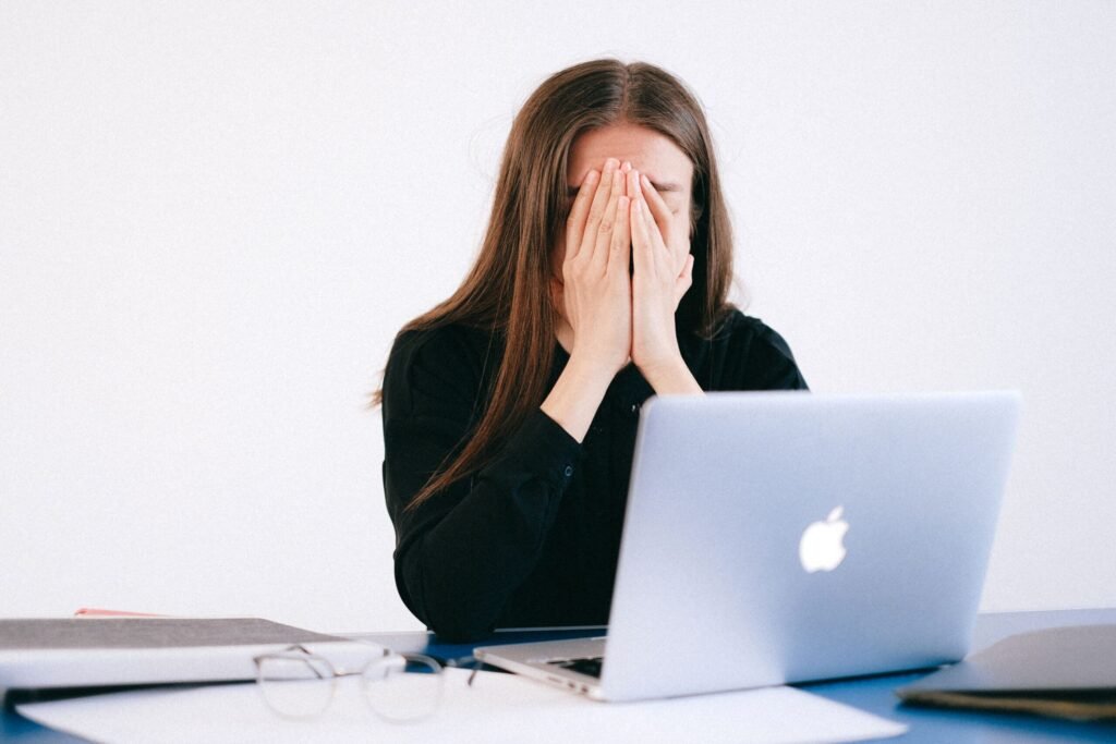 Woman feeling stressed and overwhelmed at her desk while working remotely on a laptop.