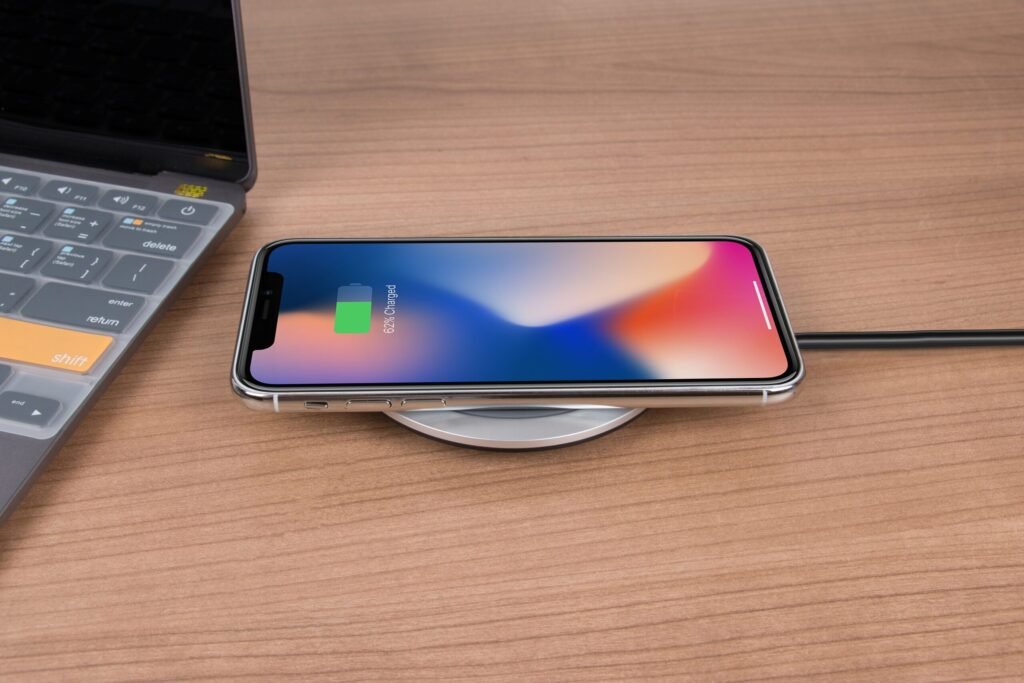 Mobile phone charging wirelessly on a desk next to a laptop, showcasing modern technology.